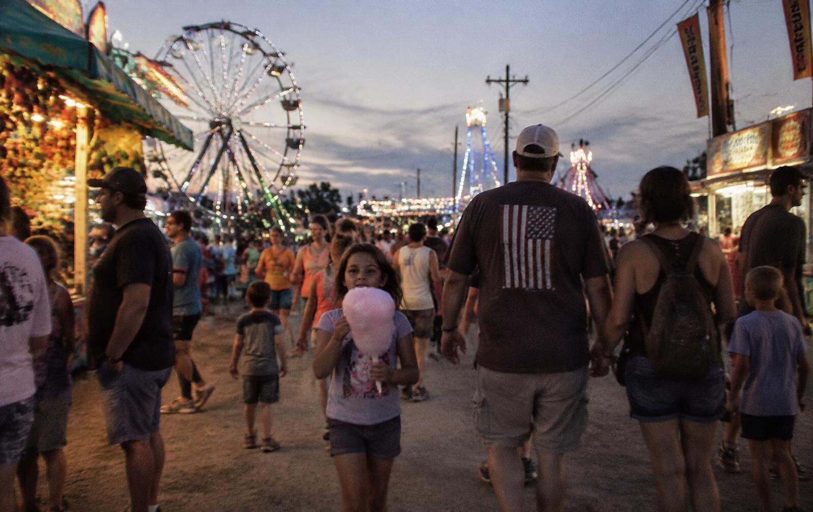 Families walking a county fair midway at dusk