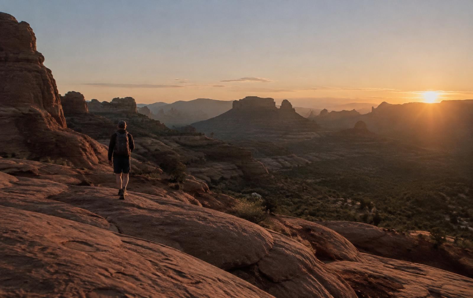 A hiker on red rocks above a desert valley at dusk